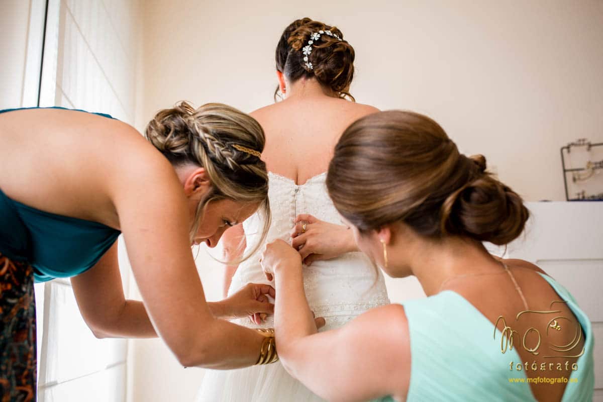 Damas de honor abrochando el vestido a la novia, detrás de ella